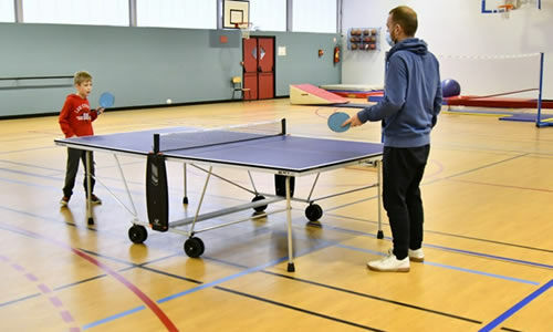 Un adulte joue au pingpong avec une enfant dans une salle de sport