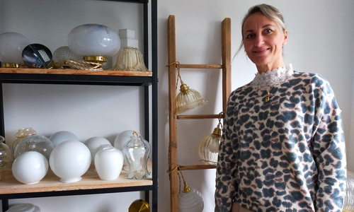 Nous voyons la créatrice de Bigsy : Madame Turquin Bigo à droite, souriante à côté de ses créations décoratives : vases, lampes, luminaires et autres types d'éclairage