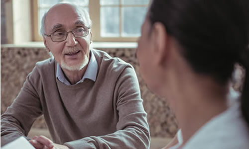 Un homme senior avec des lunettes parle avec une personne de dos