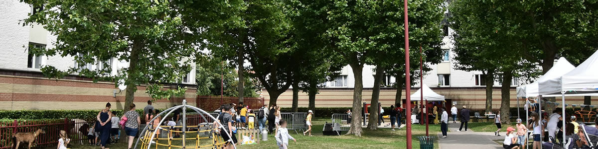 Une fete de quartier avec des enfants et des tonnelles au milieu d'un espace vert entouré d'immeubles bas