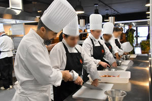 école de cuisine, un chef avec une toque, apprend à utiliser un couteau pour émincer des légumes couper des carottes à une élève