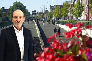 Jean Louis Munch , un homme avec une veste de costume bleu marine se tient le devant le grand boulevard ou des personnes se promènent. Des fleurs rouges au premier plan droit sont également présentes