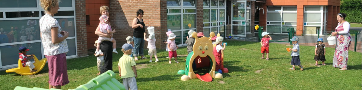 Des jeunes enfants jouent sur une pelouse encadrés par des assistantes maternelles