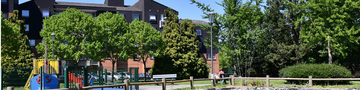 Vue d'un parc avec un jet d'eau au premier plan et des appartements de 4 étages en fond