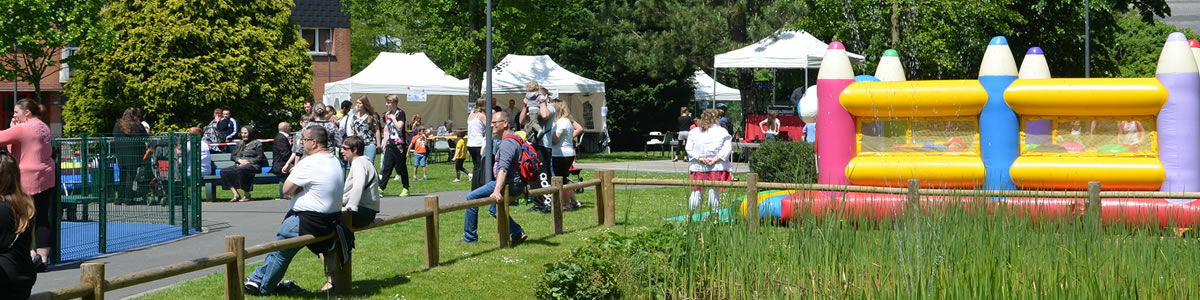 Une fête avec un château gonflable et de l'herbe au premier plan dans le parc Philippe Noiret, des personnes sont posées une barrière en bois, des tonnelles en fond d'image